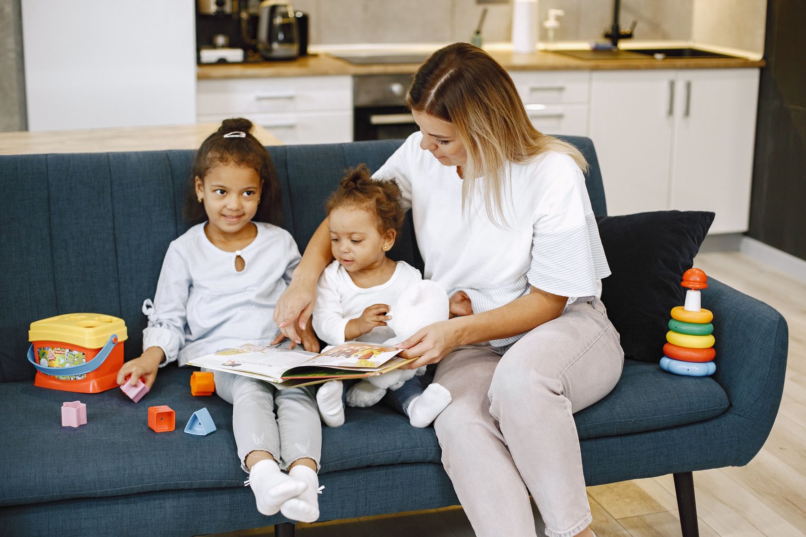 Una sitter legge un libro illustrato con due bambine sul divano